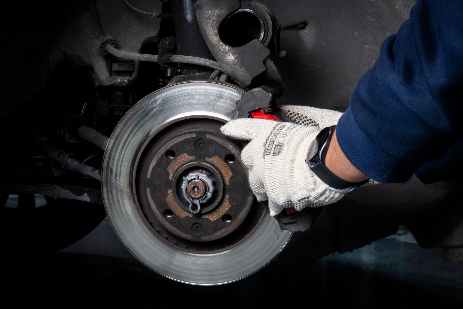 Gloved mechanic working on brake pads beside an exposed brake rotor