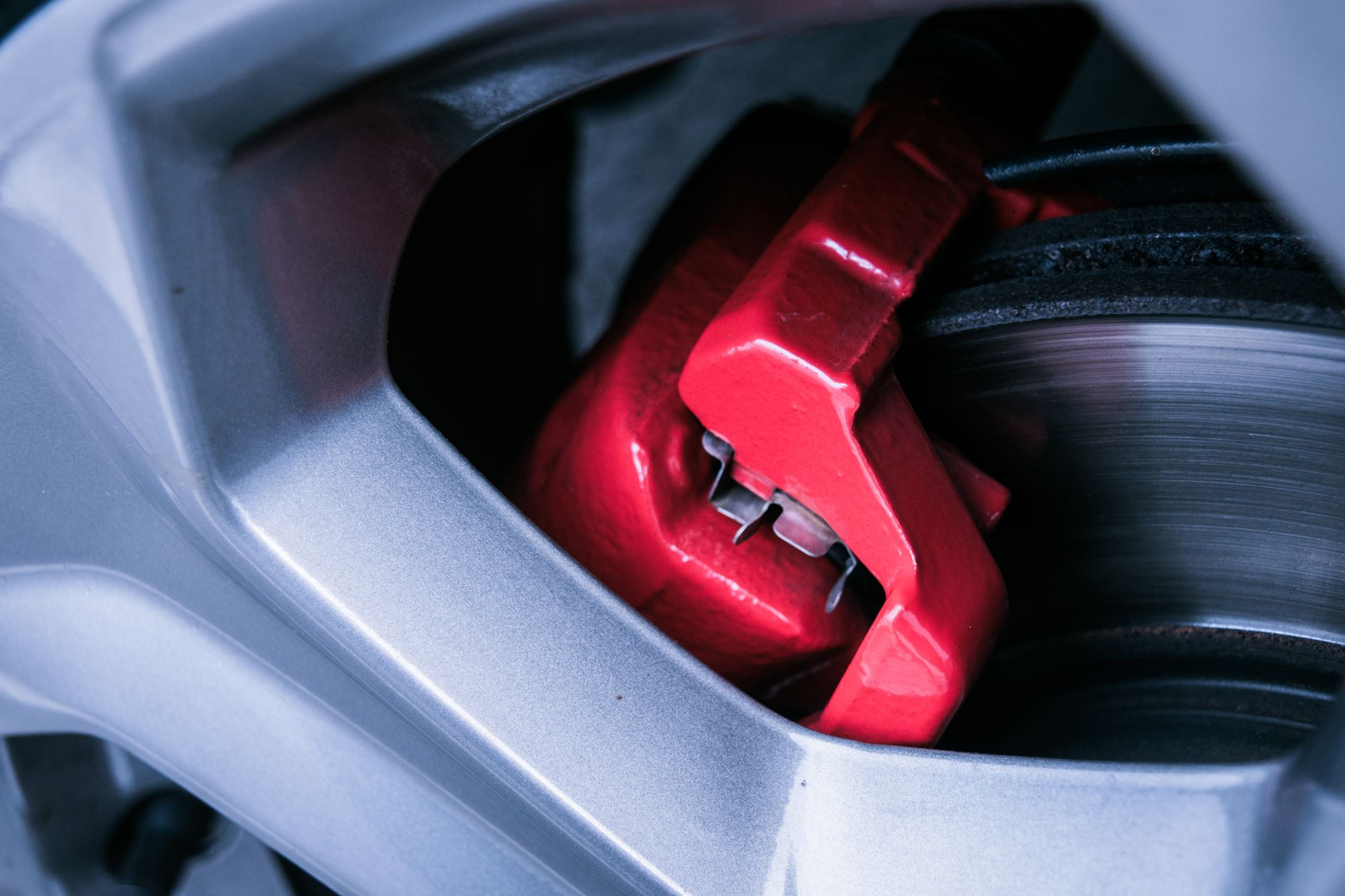 Close-up of a red brake caliper and metal brake rotor behind a wheel
